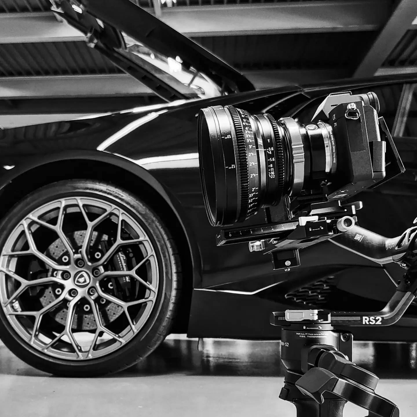 Caméra de cinéma devant une jante de sportive, en noir et blanc